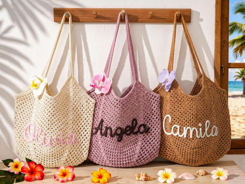 Puede incluir: Tres bolsos de ganchillo colgados en un perchero de madera. El bolso crema lleva el nombre Olivia, el bolso malva lleva el nombre Angela y el bolso marr&oacute;n lleva el nombre Camila. Cada bolso est&aacute; adornado con una flor de orqu&iacute;dea artificial.