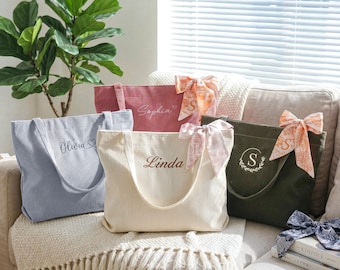 May include: Five corduroy tote bags in various colors: light blue, pink, cream, and olive green. Each bag has a name embroidered on it, such as "Olivia" and "Linda". The bags are decorated with patterned bows.