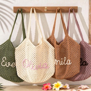 Puede incluir: Cuatro bolsos de ganchillo en verde oliva, crema, marr&oacute;n claro y rosa polvoriento colgados en un perchero de madera. Cada bolso presenta un patr&oacute;n de malla abierta y un nombre personalizado en letra cursiva: Eve, Olivia, Mila y otro.