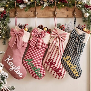 Könnte beinhalten: Vier Weihnachtsstrümpfe hängen an einer Holzleiste. Der erste ist altrosa mit passender Schleife und dem weißen Namen Kaylee. Der zweite ist rot-weiß kariert mit Schleife und dem grünen Namen Amelia. Der dritte ist rot-weiß gestreift mit Schleife und dem roten Namen Blake. Der vierte ist marineblau-weiß kariert mit Schleife und dem gelben Namen Declan.