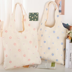 K&ouml;nnte beinhalten: Zwei beigefarbene Einkaufstaschen mit Blumenmustern. Eine Tasche hat rosa Blumen und die andere hat blaue Blumen.