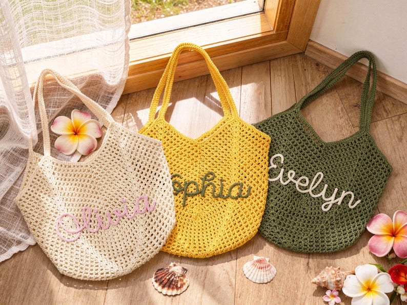 Puede incluir: Tres bolsos de ganchillo en color crema, amarillo y verde oliva. Cada bolso presenta un dise&ntilde;o de malla abierta con dos asas y un nombre personalizado bordado en letra cursiva en la parte delantera: Olivia en rosa, Sophia en verde y Evelyn en blanco.