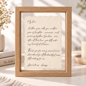 May include: A light oak wood floating frame containing a piece of cream-colored paper with deckled edges. The paper features black cursive text that reads: My love, Another year with you another year of laughter, memories, and growing together.