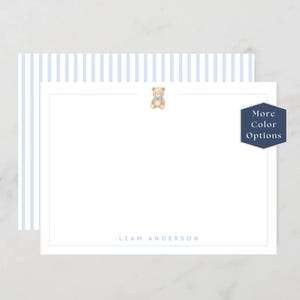 May include: White stationery with a light blue border and a light blue striped pattern on the top left. A small teddy bear illustration is at the top center. The name "LIAM ANDERSON" is printed at the bottom. A navy blue hexagon with "More Color Options" is on the right.