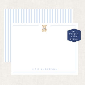 May include: A white stationery card featuring a light blue striped border, a small illustration of a tan teddy bear with a blue bow at the top center, and the name LIAM ANDERSON printed in light blue at the bottom, with a dark blue badge.