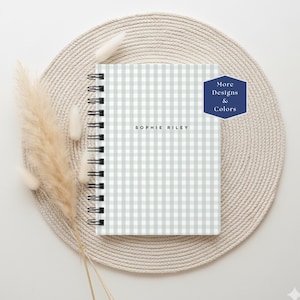 May include: A spiral-bound notebook featuring a light sage green and white gingham check pattern. The cover is personalized with the name SOPHIE RILEY in black sans-serif text. A dark blue hexagon badge in the top right corner reads More Designs & Colors.