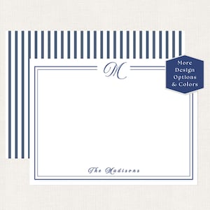 May include: A white stationery card with a navy blue striped border and a navy blue double-line frame. The card features a central navy blue script letter M monogram at the top and the text The Madisons at the bottom. A blue hexagon badge reads More Design Options & Colors.