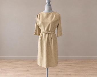 May include: A beige knee-length dress with three-quarter length sleeves, a round neckline, and a matching belt at the waist. The sleeves feature small buttons at the cuffs, and the dress has a subtle textured pattern throughout the fabric.
