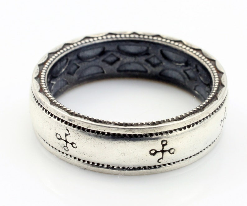 K&ouml;nnte beinhalten: Ein silberfarbener Ring mit einem eingravierten Design. Der Ring hat ein Band mit kreuzartigen Symbolen und einem detaillierten Rand. Der innere Teil des Rings hat ein strukturiertes Muster. Ein klassisches Schmuckst&uuml;ck.