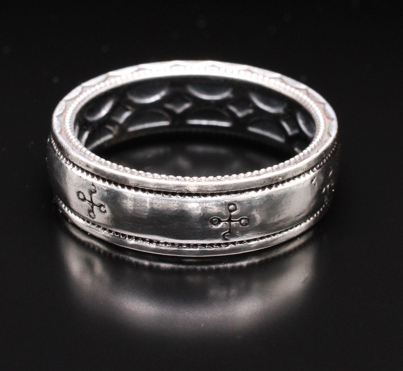 K&ouml;nnte beinhalten: Ein silberner Ring mit detailliertem Design. Der Ring hat ein Band mit kreuzartigen Symbolen und einem strukturierten Muster. Der Ring hat eine Breite von ca. 0,8 cm.