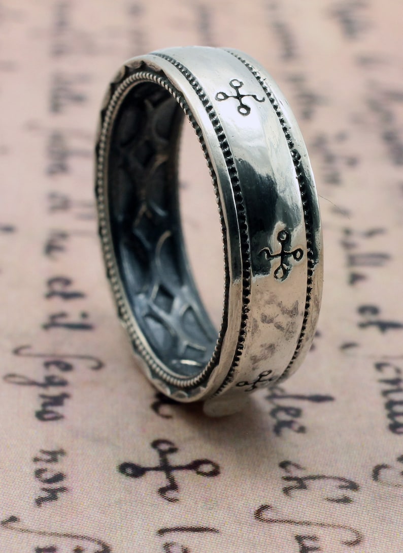K&ouml;nnte beinhalten: Ein silberner Ring mit strukturierter Oberfl&auml;che und eingravierten Kreuzsymbolen. Der Ring hat ein detailliertes Design mit einem Band aus kleinen Punkten und einem Innenmuster. Der Ring ist wahrscheinlich aus Sterlingsilber.