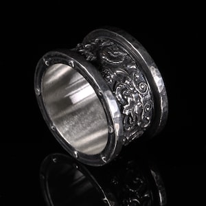 Puede incluir: Un anillo de plata con un intrincado diseño floral. El anillo es ancho y tiene una textura martillada.