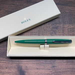 May include: A green pen with silver accents in a white box with the word "ROLEX" printed on the lid.