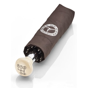 May include: A brown umbrella with a silver handle and a white gear shift knob. The umbrella has the Mercedes-Benz logo on it.