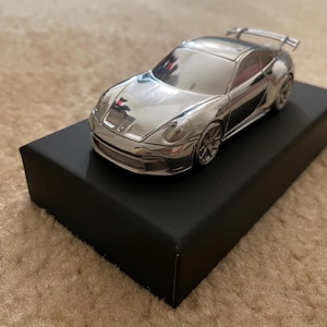 Puede incluir: Un coche de modelo plateado en una caja de exhibición negra. El coche es un Porsche 911 GT3 RS.