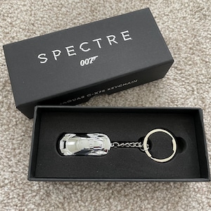 May include: A silver Jaguar C-X75 keychain in a black box with the text "SPECTRE 007 JAGUAR C-X75 KEYCHAIN" on the top.
