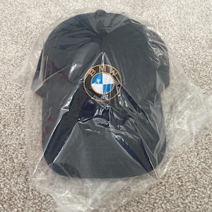 Op de afbeelding: Een zwarte baseballpet met een geborduurd BMW-logo in wit en blauw op de voorkant.