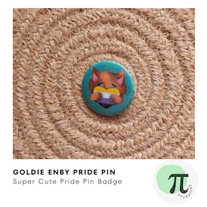 Può includere: Una spilla a bottone blu turchese con una volpe dei cartoni animati che tiene un cuore con i colori della bandiera del pride non binario. Il testo "Goldie Enby Pride Pin" e "Super Cute Pride Pin Badge" è sotto l'immagine.