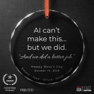 May include: A clear crystal glass ornament with an orange ribbon. The ornament has the text "Al can't make this... but we did. And we did a better job." It also says "Happy Boss's Day October 16, 2026" and lists names.