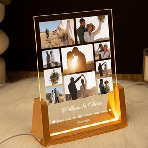 May include: A wooden photo frame with a clear acrylic insert displaying a collage of nine photos of a couple. The frame has a warm glow and the text "William & Olivia Love you to the moon and back 02-03-2023" is engraved on the bottom.