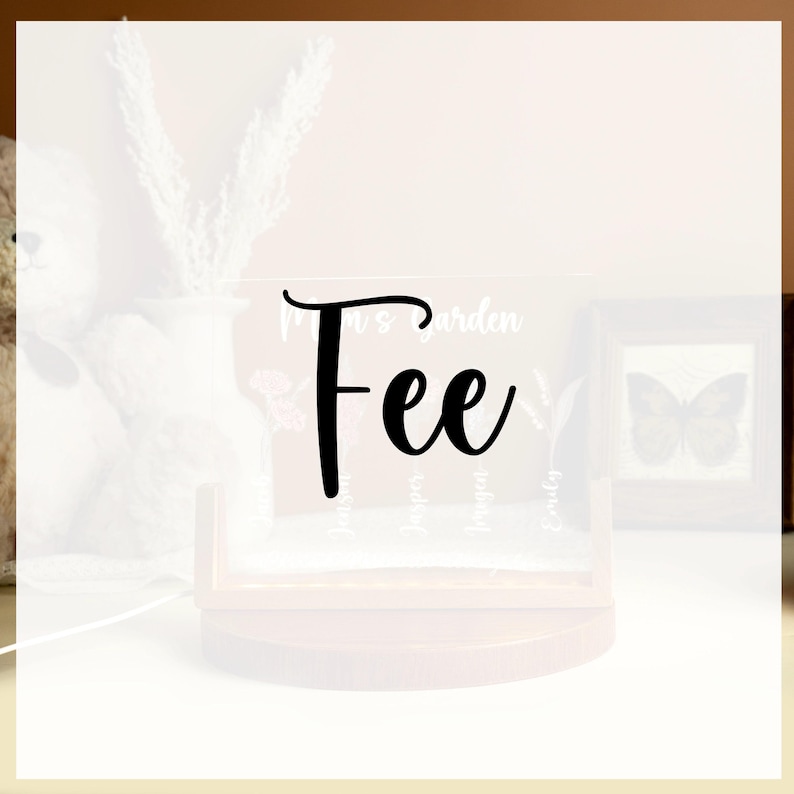 May include: A personalized acrylic night light with the word "Fee" in a bold, black script. The light is set on a wooden base and features the text "Mom's Garden" and names. A framed butterfly is in the background.