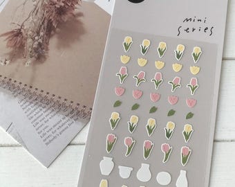 May include: A sheet of stickers with a variety of pink, yellow, and green tulip flower designs. The stickers are arranged in rows and columns on a white background. The text "mini series" is printed in black at the top of the sheet.
