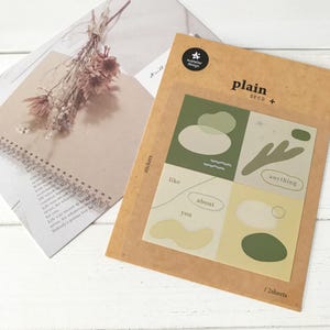 May include: A pack of stickers with a green, beige, and yellow abstract design. The stickers feature the words "like", "about", "you", and "anything". The pack contains 2 sheets of stickers.