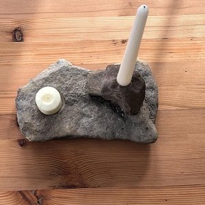 May include: A stone candle holder with two candle slots. One slot holds a white pillar candle and the other holds a white tea light candle.