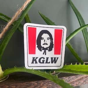 May include: A white sticker with a red and white background featuring a black and white illustration of a person with a mustache and a bow tie. The text "KGLW" is printed in black below the illustration.