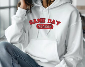 Op de afbeelding: Witte hoodie met de tekst "GAME DAY SEASON" in rode letters.