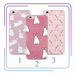 May include: Three different phone cases with a pink background and white bunny rabbit designs. The first case has a pink background with white stars and bunnies. The second case has a pink background with a white diamond pattern and bunnies. The third case has a pink background with white bunnies and orange carrots.