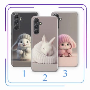 May include: Three phone cases with different cute animal designs. The first case features a white bunny wearing a gray scarf and hat. The second case features a white bunny sleeping with its head tucked into its paws. The third case features a pink bunny wearing a pink hat and scarf.