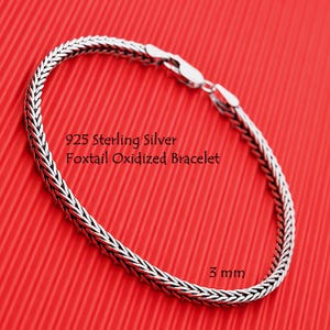 May include: A 925 sterling silver foxtail oxidized bracelet with a 3 mm width. The chain features a woven, textured link design and a polished silver lobster claw clasp. The text 925 Sterling Silver Foxtail Oxidized Bracelet and 3 mm is visible.