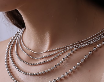 May include: A layered necklace set consisting of five individual silver-toned ball chain necklaces of varying lengths. Each chain features small, uniform, polished spherical beads connected in a continuous strand, creating a cascading effect.