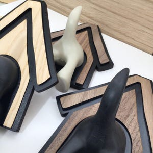 Può includere: Tre ganci in legno a forma di cane con dettagli in legno marrone e nero. I ganci hanno la forma della testa e della coda di un cane, con la testa rivolta verso il muro. I ganci sono progettati per essere montati su una parete.