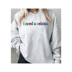 May include: A light gray sweatshirt with the phrase "i need a celsius" printed across the chest in rainbow-colored letters. The sweatshirt has long sleeves and a crew neck.