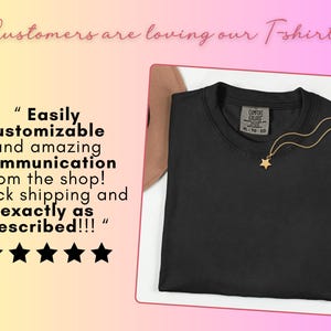 May include: A solid black crew neck t-shirt with a Comfort Colors label in size XL. A gold-toned necklace with a small star pendant rests on the neckline. The image includes text stating Customers are loving our T-shirts and a five-star review.