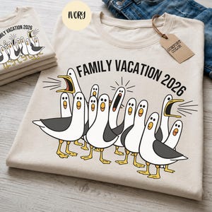 May include: An ivory t-shirt featuring a graphic of multiple white and grey seagulls with yellow beaks and feet. Some seagulls have open beaks as if squawking. The text "FAMILY VACATION 2026" is printed in black above the seagull illustration.