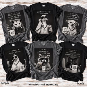 May include: Six short-sleeved t-shirts in black and charcoal gray, each featuring a black-and-white graphic of an animal in an office setting with humorous text. Animals include an opossum, duck, chihuahua, chicken, raccoon, and cat.