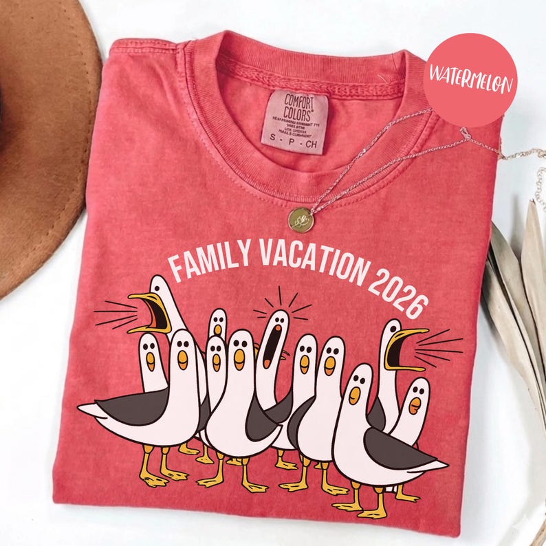May include: A watermelon-colored t-shirt featuring a graphic of multiple white and grey seagulls with yellow beaks and feet. The text "FAMILY VACATION 2026" is printed in white above the birds. The shirt has a Comfort Colors brand label at the neck.