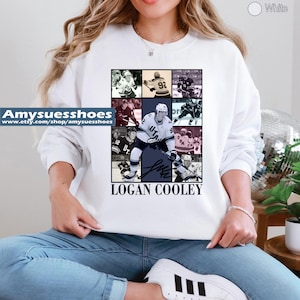 May include: White sweatshirt with a collage of hockey player images and the name "LOGAN COOLEY" in black. The design includes a signature and the text "UT". A casual item of clothing.