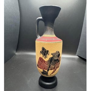 May include: A ceramic vase with a black handle and rim, featuring a beige body with a red and yellow band. The vase is decorated with black and red figures, and rests on a black base. The vase has a height of approximately 8 inches.