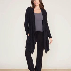 Könnte beinhalten: Ein schwarzer Cardigan mit langen Ärmeln, einem drapierten Vorderteil und Taschen. Der Cardigan wird über einem grauen Tanktop und einer schwarzen Hose getragen.