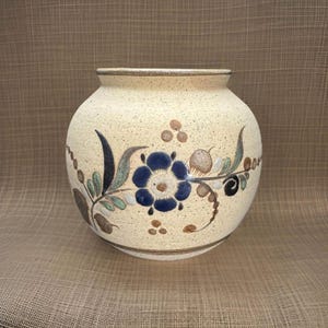 May include: A cream-coloured ceramic vase with a speckled finish and a floral design in shades of blue, green, and brown.