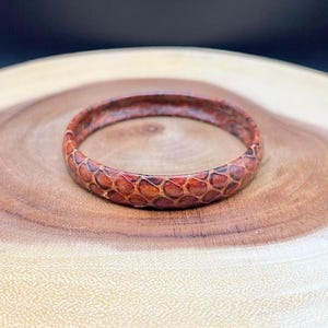 Może przedstawiać: Bransoletka skórzana w kolorze brązowym z wzorem skóry węża.