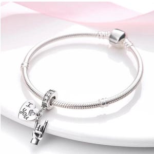 May include: A silver bracelet with a charm that says "I You" and a hand gesture charm. The bracelet is on a white surface. The bracelet is made of a silver metal.