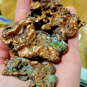 May include: A collection of three rough, copper nuggets with a green patina. The nuggets are irregular in shape and have a metallic sheen.