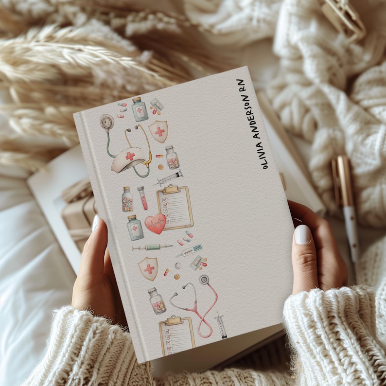 May include: A cream-coloured notebook featuring a medical-themed illustration on the left. The design includes a stethoscope, medical bottles, a heart, and a clipboard. The text "OLIVIA ANDERSON RN" is printed vertically on the right side.