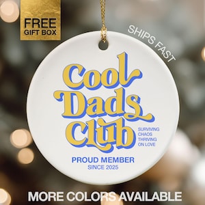May include: White ceramic ornament with the text "Cool Dads Club" in yellow and blue. The ornament also includes the phrases "Proud Member Since 2025" and "Surviving Chaos Thriving on Love". A gold cord is attached for hanging.