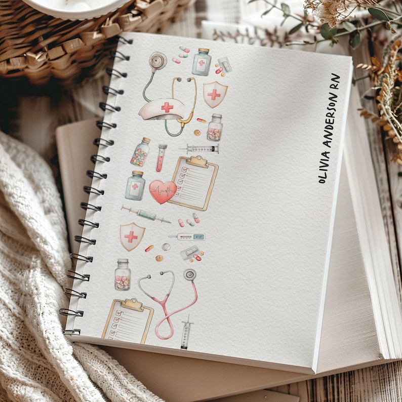 May include: A white spiral-bound notebook with a medical-themed watercolour design. The design includes a stethoscope, pills, syringes, and a nurse's hat. The name "OLIVIA ANDERSON RN" is printed vertically on the right side of the notebook.